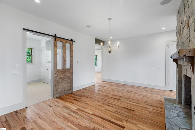 621 Bascule Ridge Ln, Campobello, SC 29322 - unfurnished living room featuring a barn door, light wood-style flooring, a stone fireplace, recessed lighting, and a chandelier