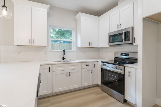 166 Dunbar St, Wellford, SC 29385 - kitchen with stainless steel appliances, white cabinetry, light wood finished floors, tasteful backsplash, and hanging light fixtures