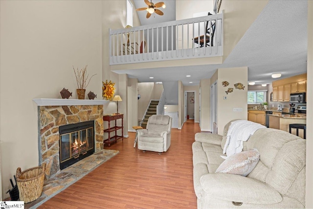 701 Loran Pointe Pointe, Seneca, SC 29672 - living room featuring light wood-style flooring, ceiling fan, a stone fireplace, stairway, and a high ceiling