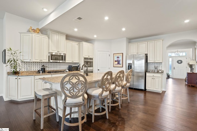 506 Bellot Winds Dr, Duncan, SC 29334 - kitchen featuring stainless steel appliances, arched walkways, tasteful backsplash, light stone countertops, and an island with sink