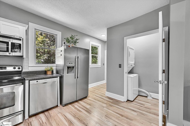 23 Stringer St, Belton, SC 29627 - kitchen with appliances with stainless steel finishes, stacked washer / dryer, light wood finished floors, white cabinetry, and a textured ceiling