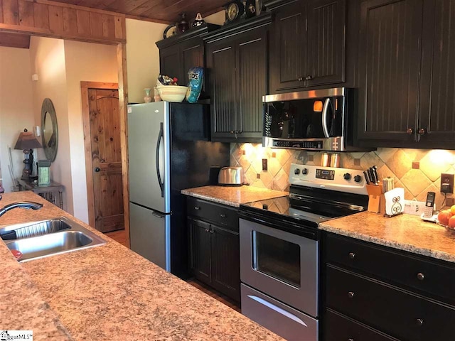 kitchen featuring backsplash, sink, light stone counters, and stainless steel appliances