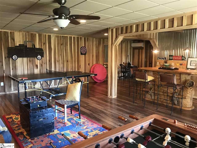 rec room featuring a drop ceiling, an AC wall unit, ceiling fan, wood walls, and dark hardwood / wood-style flooring