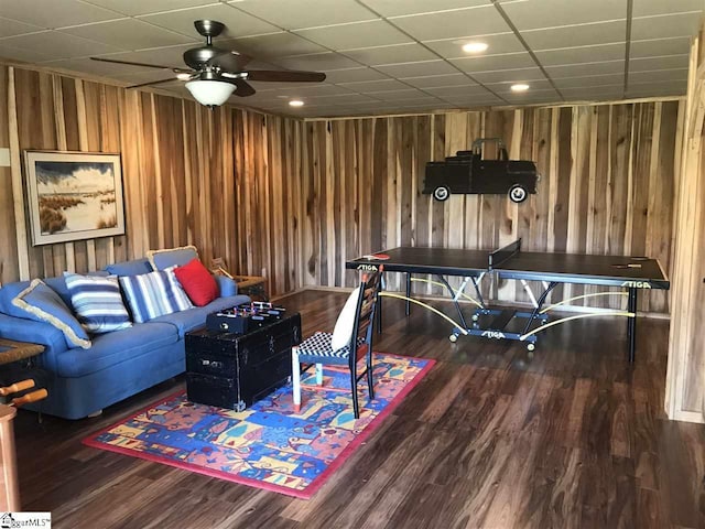 interior space with a drop ceiling, wooden walls, ceiling fan, and dark wood-type flooring