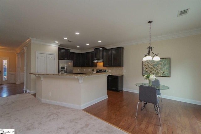 kitchen featuring stainless steel fridge, decorative light fixtures, crown molding, and light stone countertops