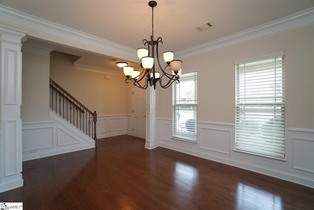 empty room featuring a chandelier, dark hardwood / wood-style floors, ornate columns, and ornamental molding