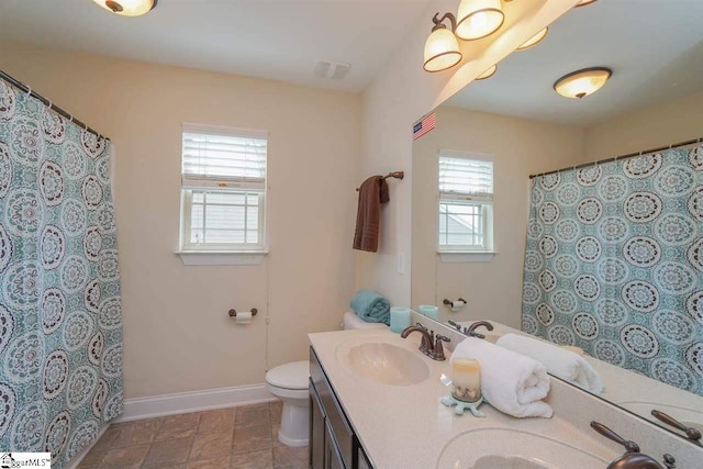 bathroom featuring dual vanity, toilet, a healthy amount of sunlight, and tile floors