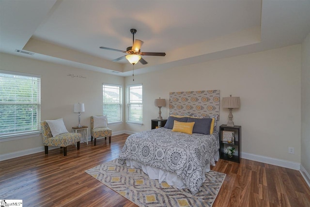 bedroom with ceiling fan, dark wood-type flooring, and a tray ceiling