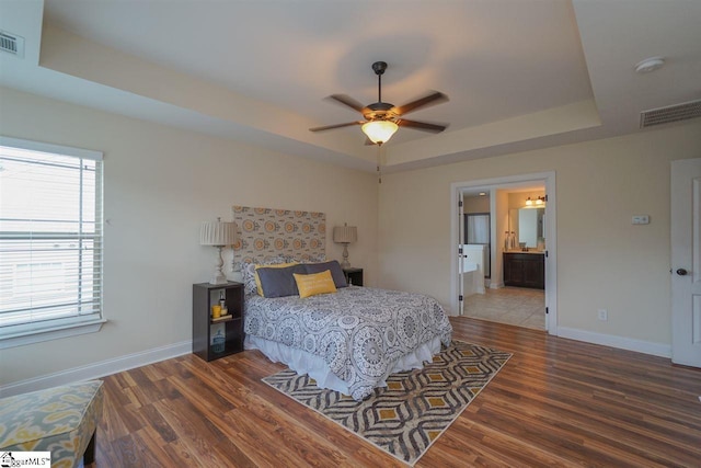 bedroom featuring a raised ceiling, dark hardwood / wood-style floors, connected bathroom, and ceiling fan