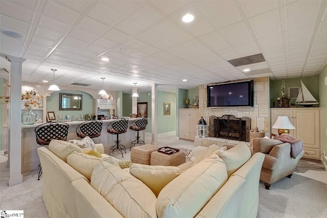 living room featuring ornate columns, a stone fireplace, and light carpet