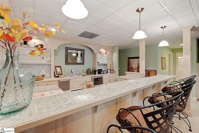 kitchen with stainless steel dishwasher, a kitchen breakfast bar, beverage cooler, hanging light fixtures, and sink