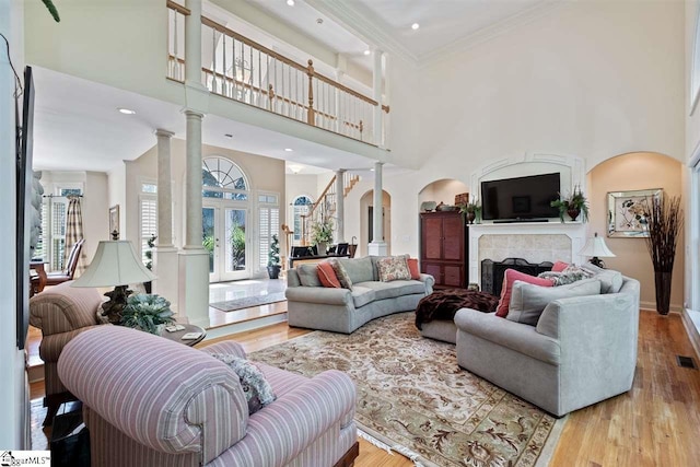 living room featuring decorative columns, light hardwood / wood-style flooring, a tile fireplace, a towering ceiling, and ornamental molding