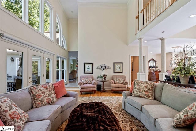 living room featuring a healthy amount of sunlight, light wood-type flooring, a towering ceiling, and ornate columns