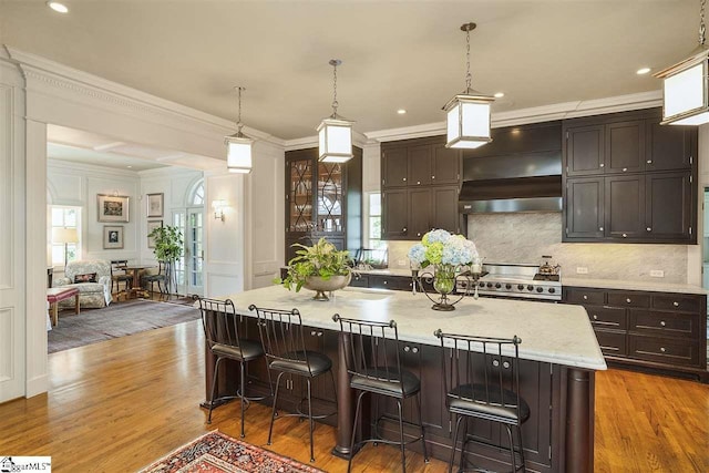 kitchen with a breakfast bar, light hardwood / wood-style floors, stove, custom range hood, and pendant lighting