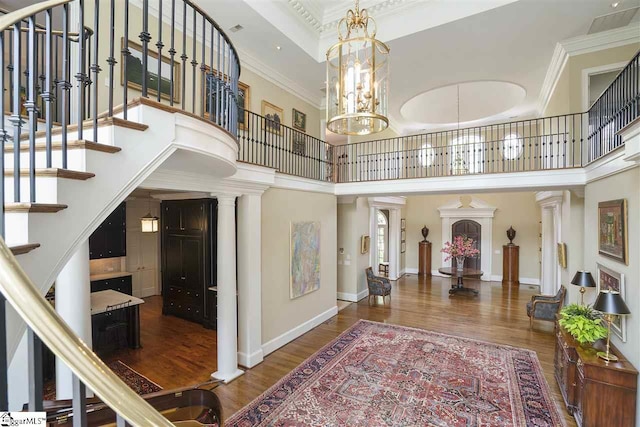 entryway with a notable chandelier, dark hardwood / wood-style flooring, crown molding, a high ceiling, and ornate columns