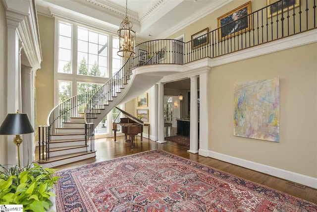 interior space featuring dark hardwood / wood-style floors, crown molding, a chandelier, decorative columns, and a high ceiling