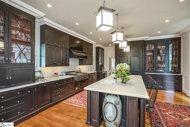 kitchen featuring double oven range, a breakfast bar, light hardwood / wood-style flooring, hanging light fixtures, and a kitchen island with sink