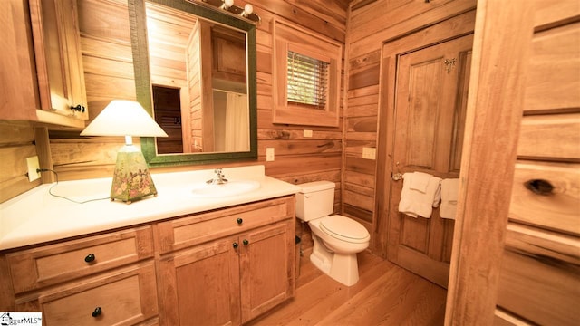 bathroom with toilet, vanity with extensive cabinet space, wood walls, and hardwood / wood-style flooring