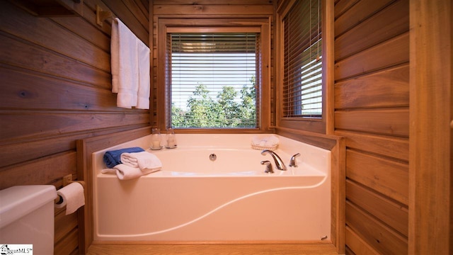 bathroom featuring wooden walls, toilet, and a bath to relax in