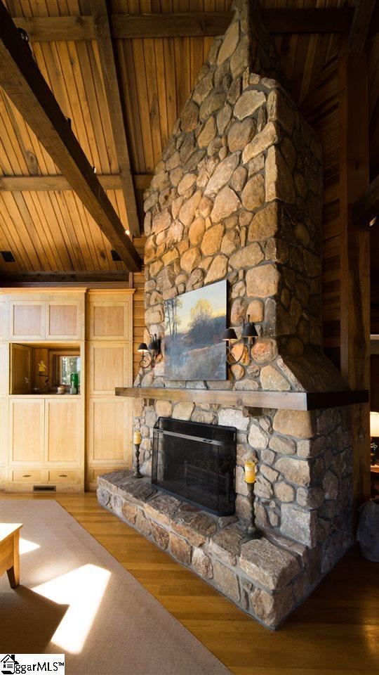 unfurnished living room featuring beamed ceiling, hardwood / wood-style flooring, a stone fireplace, high vaulted ceiling, and wood ceiling