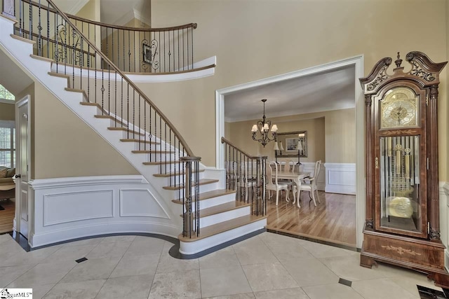 stairs with light hardwood / wood-style flooring, ornamental molding, a chandelier, and a high ceiling