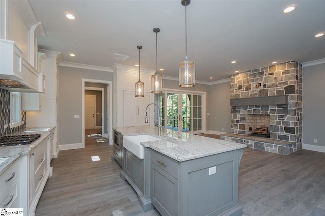 kitchen with dark hardwood / wood-style flooring, white cabinets, a center island with sink, sink, and hanging light fixtures