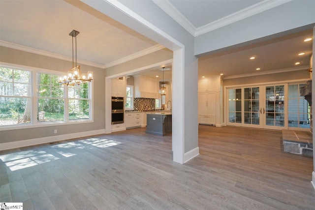 unfurnished living room with ornamental molding, a chandelier, hardwood / wood-style floors, and sink