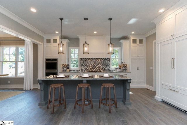 kitchen with dark hardwood / wood-style flooring, backsplash, a center island with sink, and decorative light fixtures