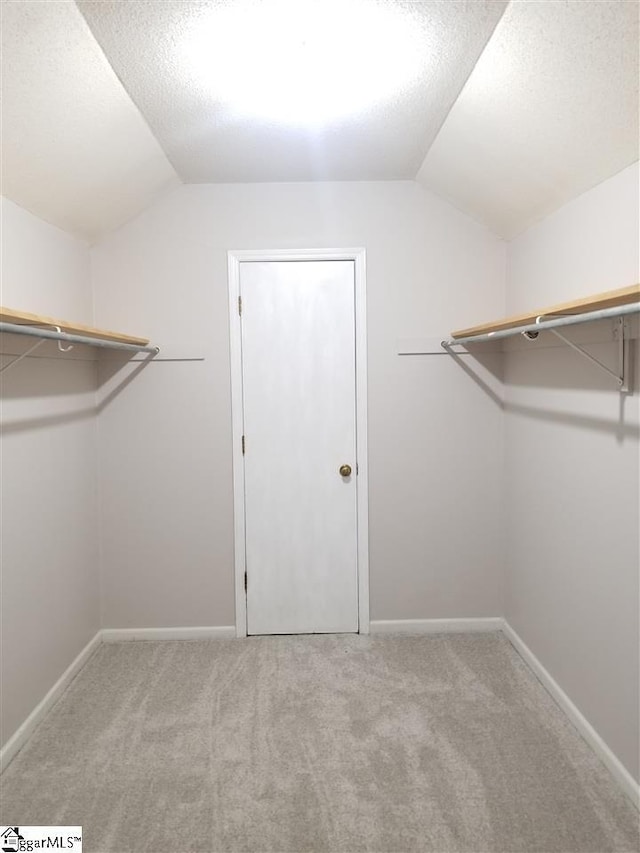 walk in closet with light carpet and lofted ceiling