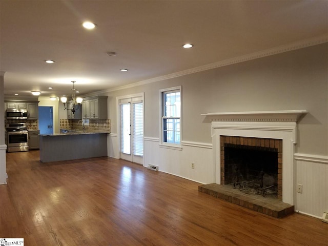 unfurnished living room with dark hardwood / wood-style floors, an inviting chandelier, sink, a brick fireplace, and crown molding