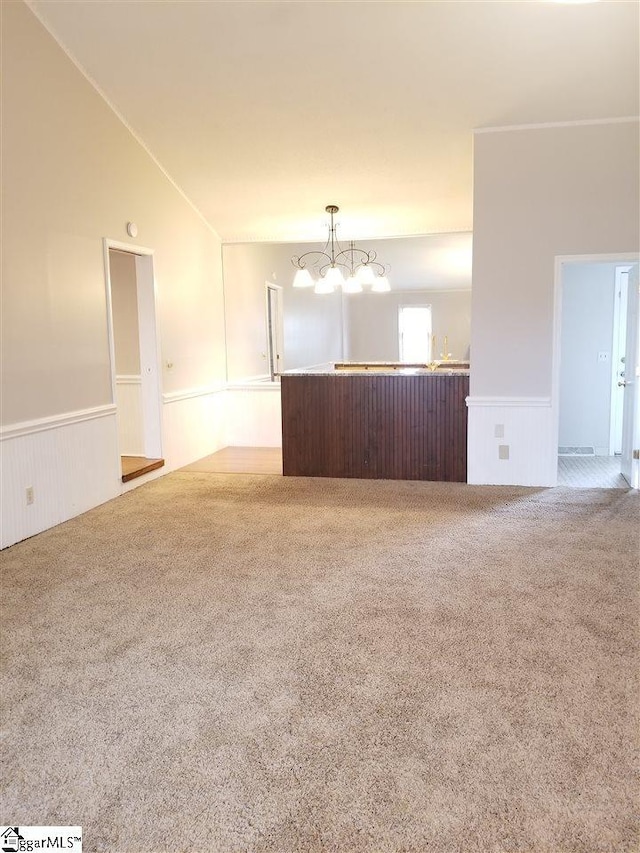 unfurnished living room with light colored carpet, vaulted ceiling, and an inviting chandelier