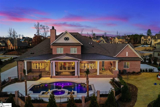 back house at dusk featuring a pool with hot tub, a lawn, and a patio