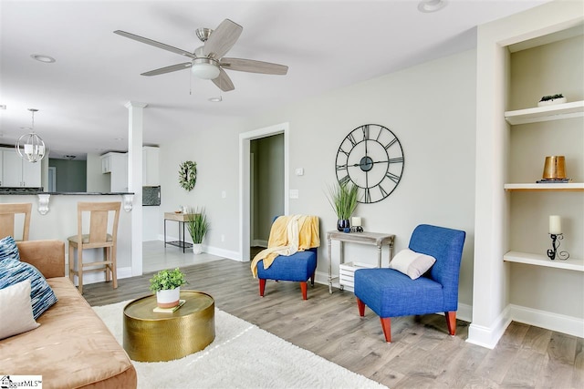 living room featuring ceiling fan with notable chandelier and light wood-type flooring