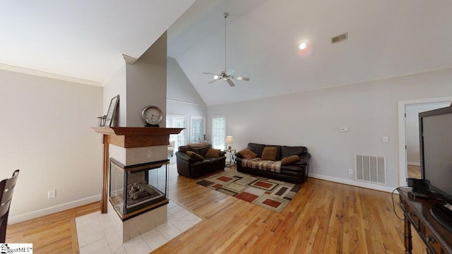 living room with ceiling fan, a multi sided fireplace, high vaulted ceiling, and light hardwood / wood-style floors