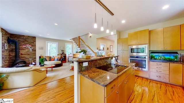 kitchen featuring pendant lighting, a wood stove, dark stone countertops, black appliances, and light wood-type flooring