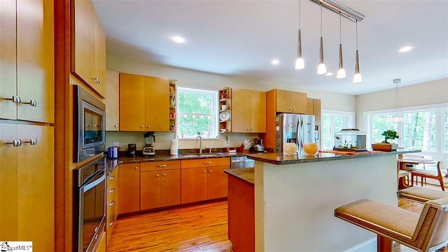 kitchen featuring appliances with stainless steel finishes, light hardwood / wood-style floors, a center island, a breakfast bar area, and pendant lighting