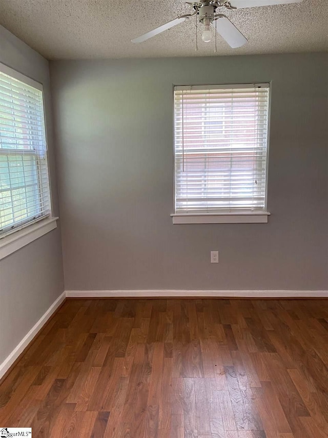 empty room with a textured ceiling, dark hardwood / wood-style floors, ceiling fan, and a wealth of natural light