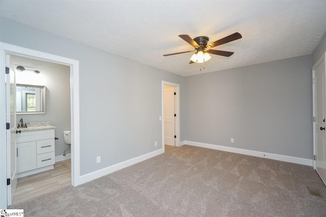 unfurnished bedroom with ceiling fan, a textured ceiling, light colored carpet, and ensuite bath