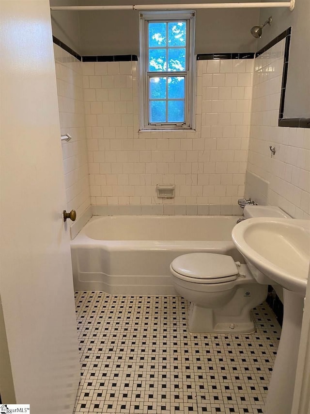 bathroom with tiled shower / bath combo, toilet, and tile flooring