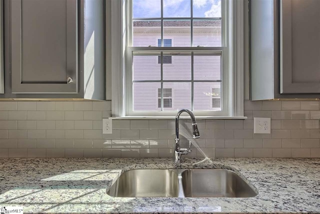 kitchen with light stone countertops, sink, and backsplash