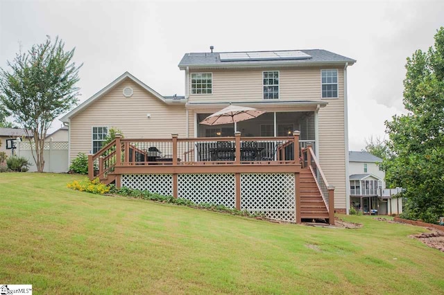 back of house with a wooden deck, solar panels, and a yard