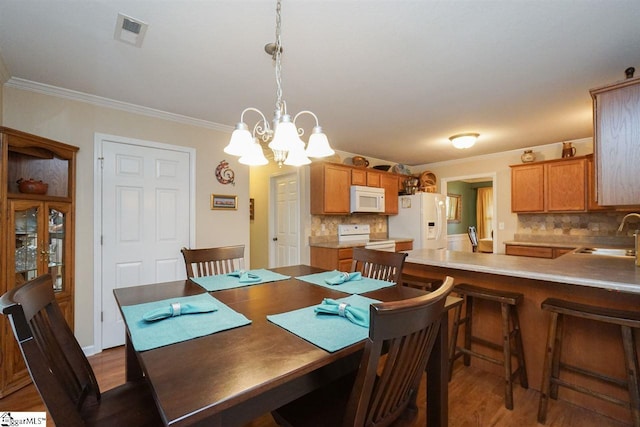 dining area with ornamental molding, a notable chandelier, sink, and light hardwood / wood-style flooring