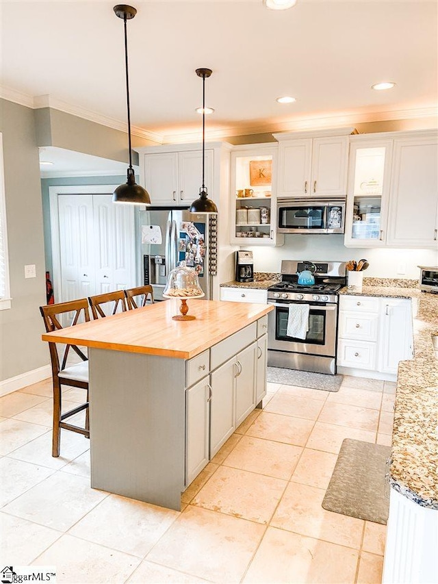 kitchen with appliances with stainless steel finishes, pendant lighting, light tile flooring, a kitchen island, and a kitchen bar