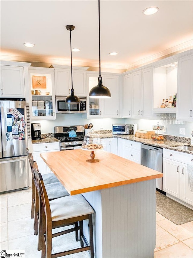 kitchen featuring light tile floors, a kitchen island, white cabinets, appliances with stainless steel finishes, and decorative light fixtures