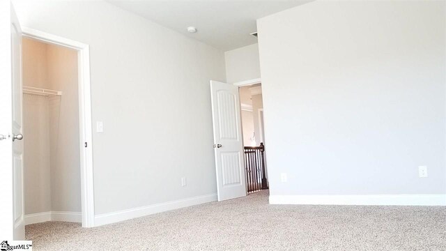 unfurnished bedroom featuring a closet, a spacious closet, and light colored carpet