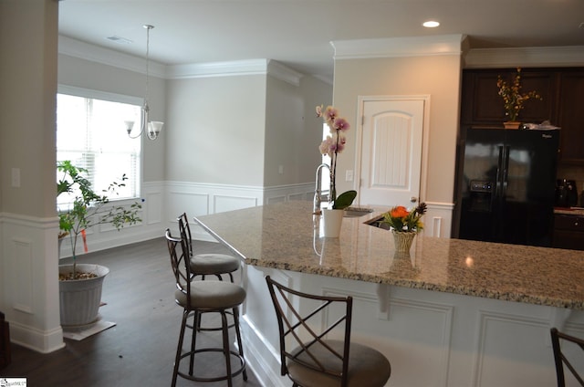 kitchen with black refrigerator with ice dispenser, a kitchen breakfast bar, sink, light stone countertops, and dark hardwood / wood-style floors