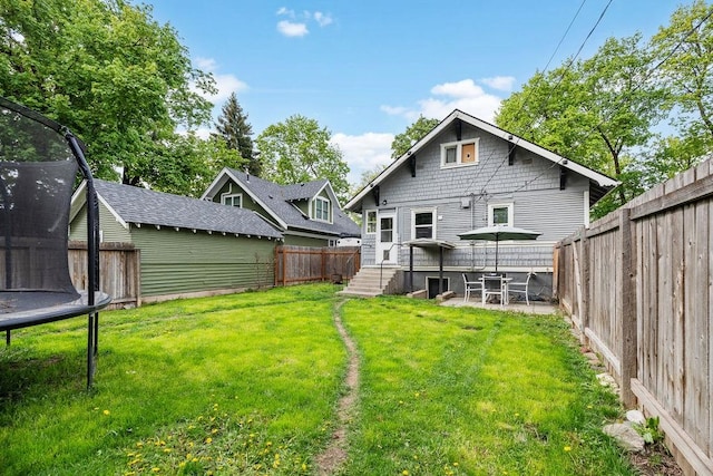 rear view of house with a patio, a trampoline, and a lawn