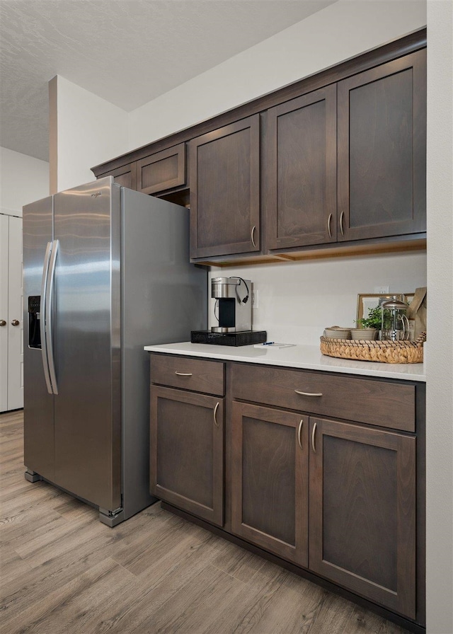 kitchen featuring light wood-type flooring, stainless steel refrigerator with ice dispenser, and dark brown cabinets