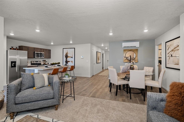 dining space with a wall mounted air conditioner, a textured ceiling, and light wood-type flooring