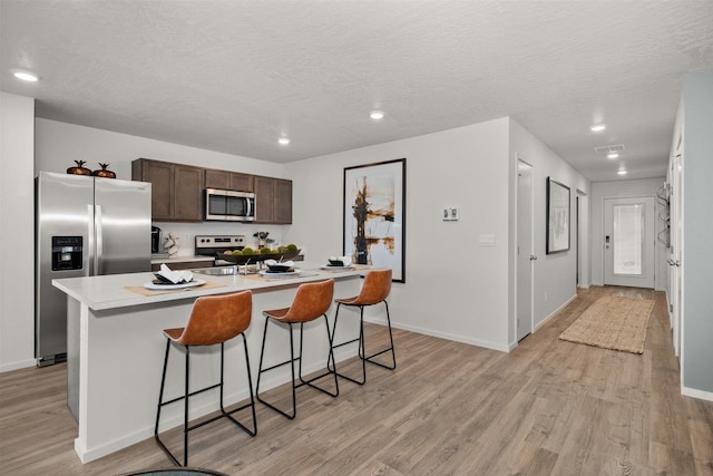 kitchen with light hardwood / wood-style flooring, a breakfast bar, dark brown cabinets, stainless steel appliances, and an island with sink